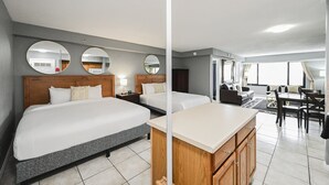 Habitación de hotel con dos camas, cabecera de madera, kitchenette, zona de comedor y baño con espejo.