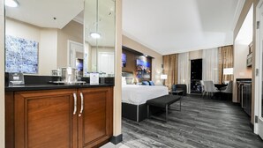 A hotel room with a bed, a desk, a chair, a small table, a mirror, a window with a cityscape view, and a kitchenette with a coffee maker. - PH Floor Studio • Strip View • Balcony • No Resort Fee D30O3 (Las Vegas)