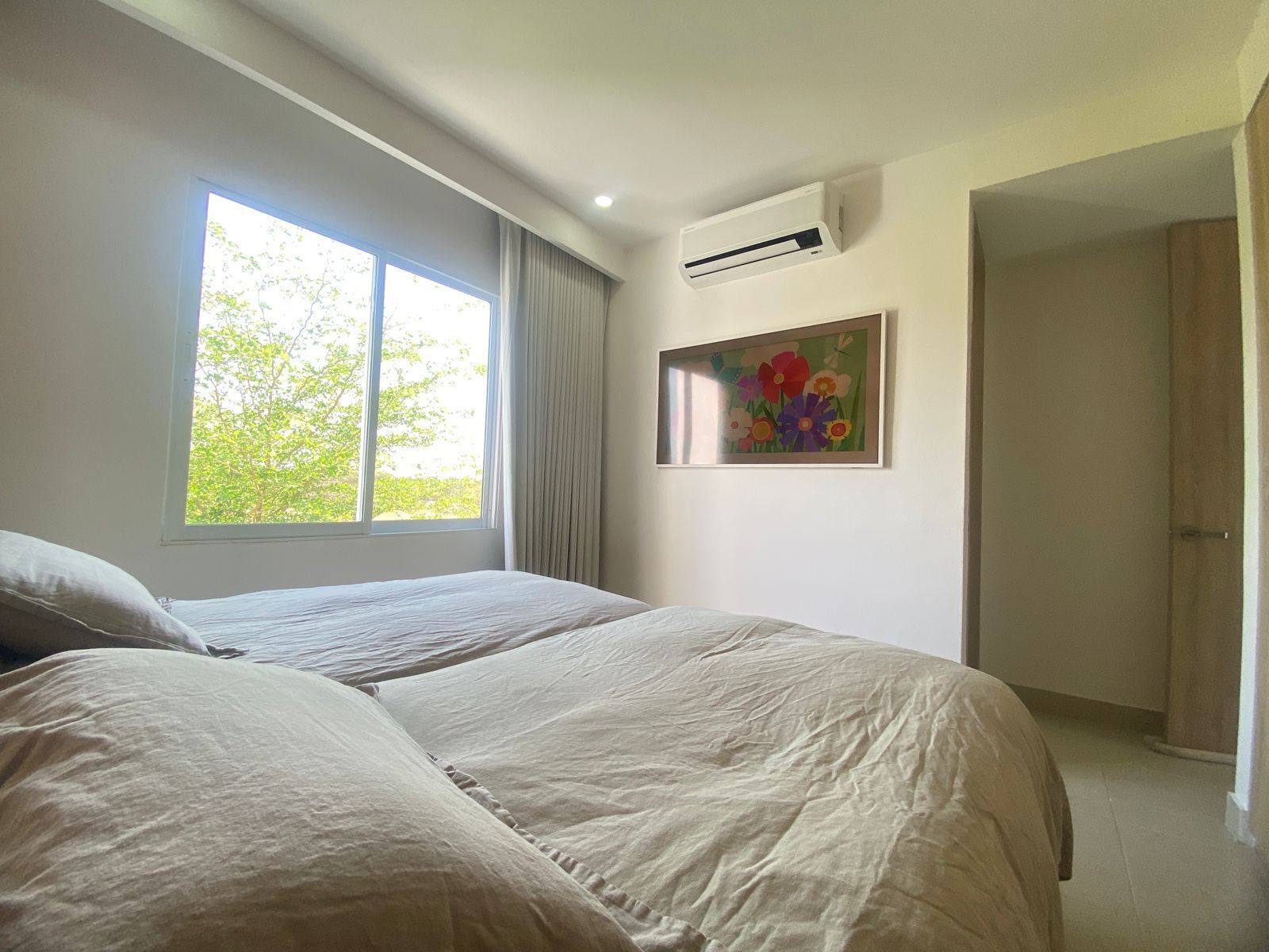 A bedroom with two beds, a window, an air conditioner, and a door.