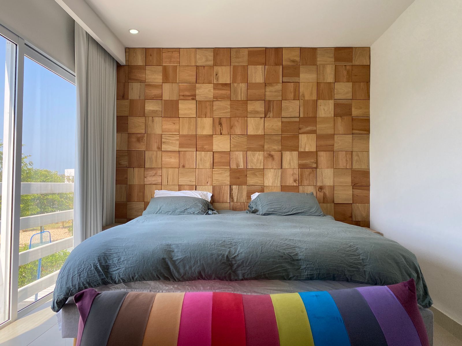 Ein Schlafzimmer mit einem hölzernen Kopfteil, einem großen Fenster und einer farbenfrohen, gestreiften Bettdecke.