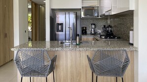 Une cuisine moderne dotée d’appareils électroménagers en acier inoxydable, de plans de travail en granit et de deux chaises en métal ajouré.