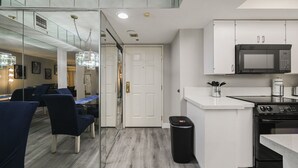 A modern kitchen with white cabinets, a microwave, and a stove. There is a dining area with blue chairs and a glass partition.
