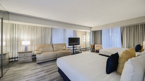 A modern hotel room with a large bed, a sofa, a TV, and a desk.