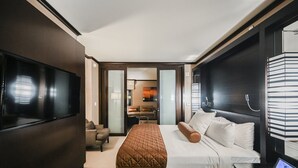 Una habitación de hotel moderna con una cama grande, un televisor de pantalla plana, una mesita de noche y vistas a la habitación contigua.