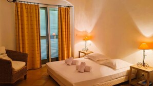 Habitación de hotel con cama, dos lámparas de noche, una silla y ventana con cortinas.