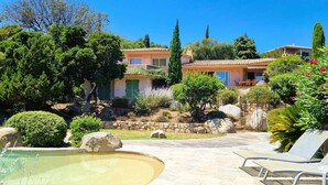 Una villa con piscina, rodeada de abundante vegetación y un camino de piedra.