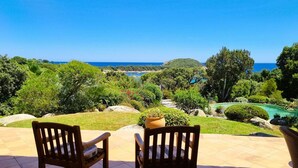 Un patio con dos sillas de madera frente a un jardín ajardinado y vistas al mar.