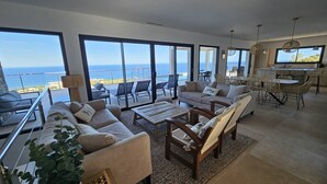 A spacious living area with large windows, a balcony, and a dining area with wicker furniture. - LABELLE- PANORAMIC SEA VIEW- PRIVATE POOL- AIR CONDITIONING-WIFI (SARI-SOLENZARA)