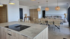 A modern kitchen with a central island, dining area with wicker chairs, and pendant lighting. - LABELLE- PANORAMIC SEA VIEW- PRIVATE POOL- AIR CONDITIONING-WIFI (SARI-SOLENZARA)