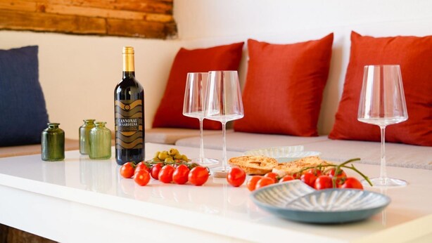 Una mesa con una botella de vino, dos copas, un plato de comida y algunos tomates.