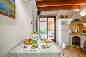 A dining area with a table set for breakfast, a kitchen with a stove and microwave, and a view of the outside. - Olbia Centro, Cala Sabina (Olbia)