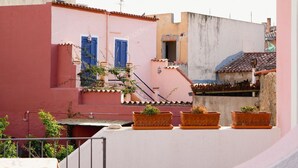 Terraza en la azotea con plantas en macetas, una escalera y edificios con estilos arquitectónicos diferentes.