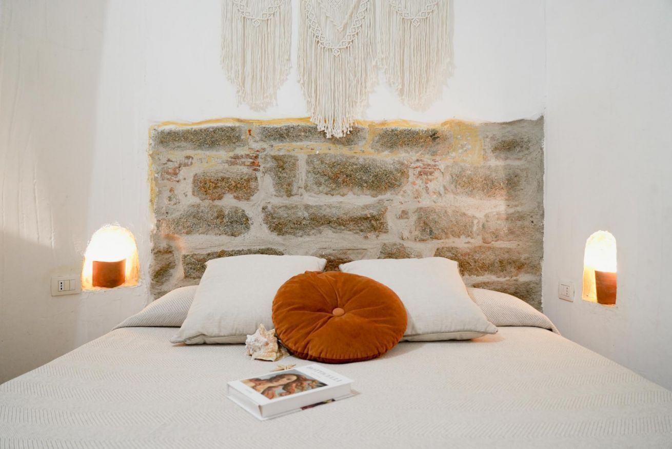 A bed with a stone headboard, two bedside lamps, and a single decorative pillow.