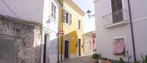 A narrow cobblestone street with buildings on either side, a stop sign, and potted plants along the right side.