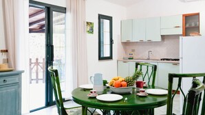 A dining area with a round table, chairs, and a bowl of fruit. There is a window with curtains, a door, and a kitchen area with cabinets and a refrigerator. - San Teodoro, Martino House (San Teodoro)