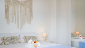 Un lit bien fait, agrémenté d’une décoration murale en macramé, d’une lampe de chevet et d’un miroir qui reflète la pièce.
