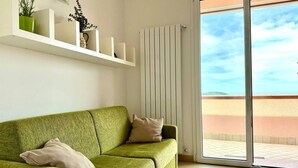 Ein grünes Sofa mit zwei Kissen, ein weißer Heizkörper und eine Glastür, die auf eine Terrasse im Freien führt.