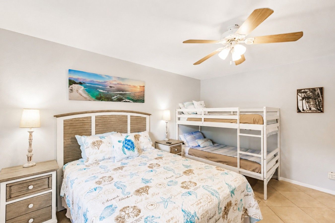 Une chambre avec un lit superposé, un ventilateur de plafond, une table de chevet avec une lampe et un tableau accroché au mur.