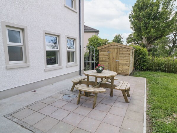 A patio with a wooden table and benches, a wooden shed, and a white building with windows. - STONEYWOOD, pet friendly, with open fire in Culdaff, County Donegal (Culduff)