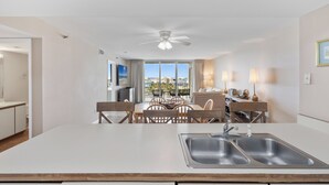 A modern kitchen with a large island, a dining area with wooden chairs, and a view of a building through large windows.