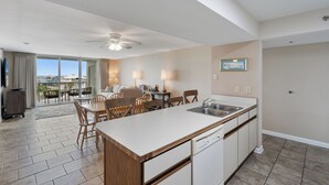 A modern kitchen with a central island, dining area with chairs, and a view to the outside.