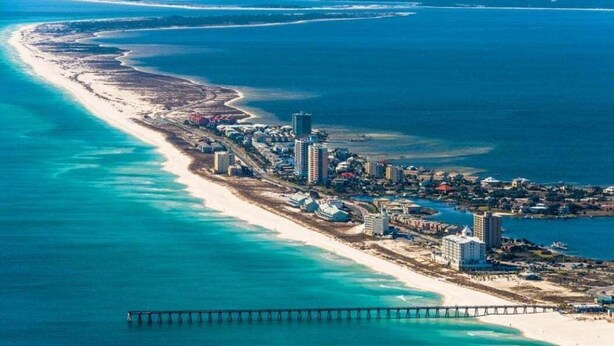 An aerial view of a coastal city with a long beach, a pier, and dense urban development.