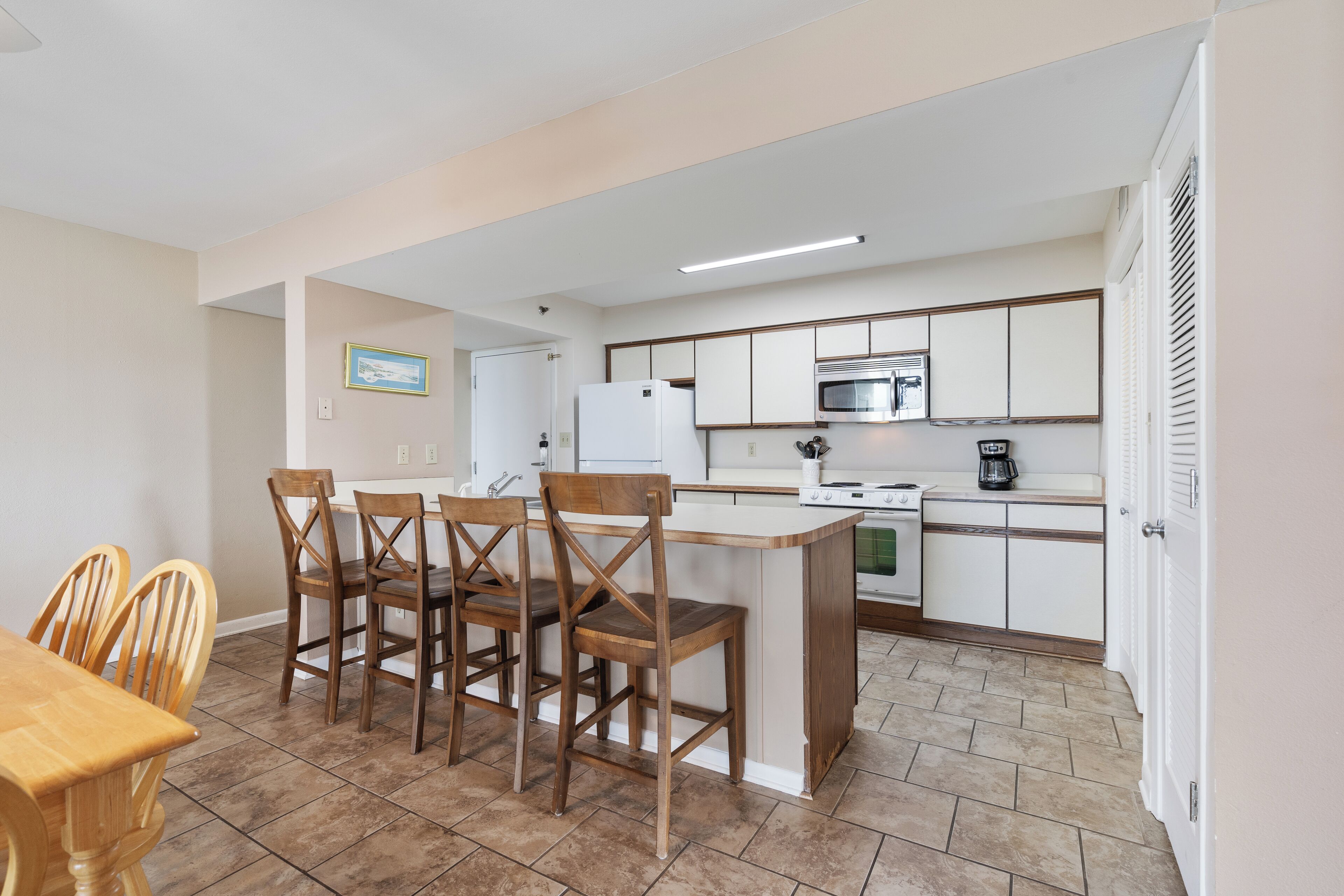 Una cocina compacta con gabinetes blancos, microondas, estufa y cafetera. Hay una mesa de comedor de madera con sillas.
