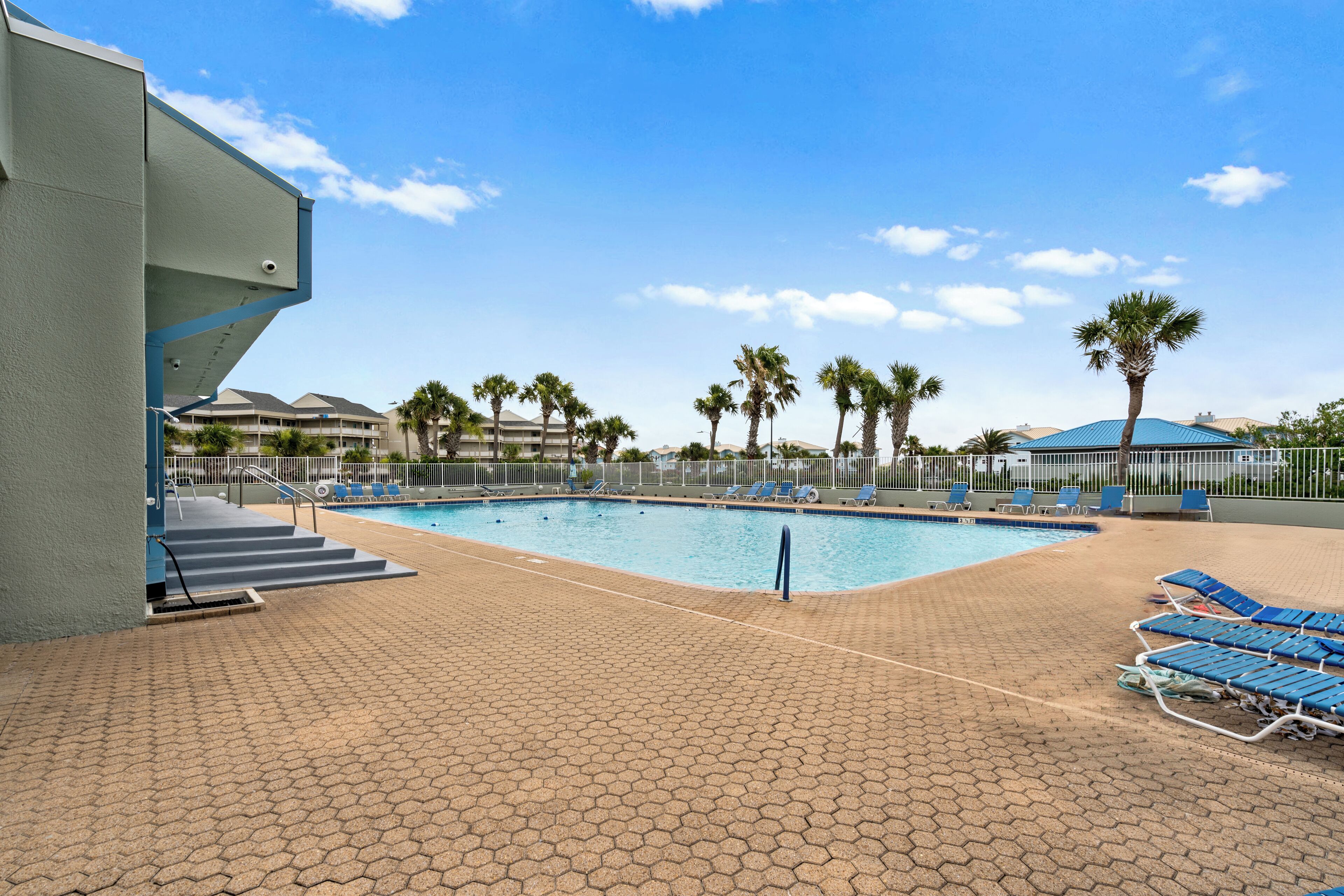 Una piscina con sillas de descanso azules y palmeras.