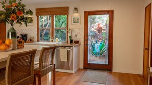 A kitchen with a dining area, a dishwasher, and a window with a view of greenery.