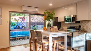 A modern kitchen with white cabinets, a built-in microwave, and a stainless steel oven. There is a dining area with a white table and wicker chairs.