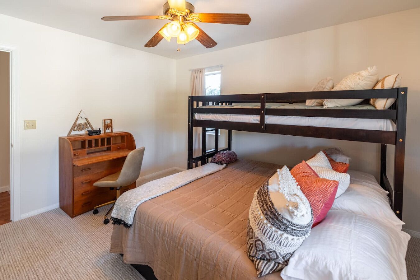 A bedroom with a bunk bed, a desk with a chair, a ceiling fan, and a window.