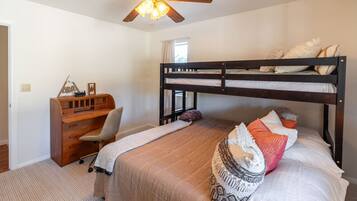 A bedroom with a bunk bed, a desk with a chair, a ceiling fan, and a window.