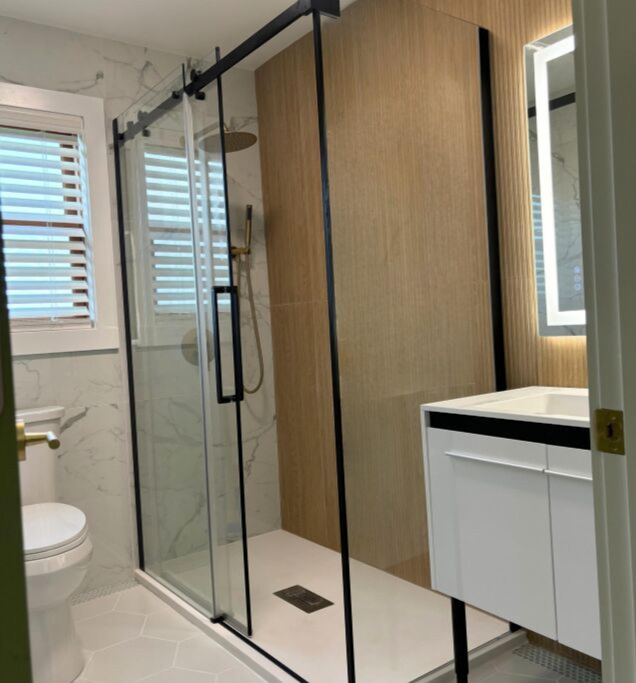 A modern bathroom with a glass shower enclosure, a white sink, and a wooden vanity.