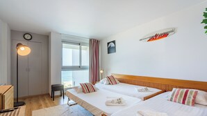 Ein Hotelzimmer mit zwei Betten, einem Schreibtisch, einem Stuhl, einer Uhr und einem fenster mit Vorhängen.