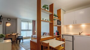 Eine kleine Küche mit Essbereich, Holzmöbeln und einbauartigen Regalen mit Pflanzen.