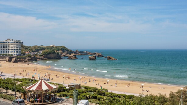 Ein Strand mit einem Karussell, sandigem Ufer und Felsen im Wasser.