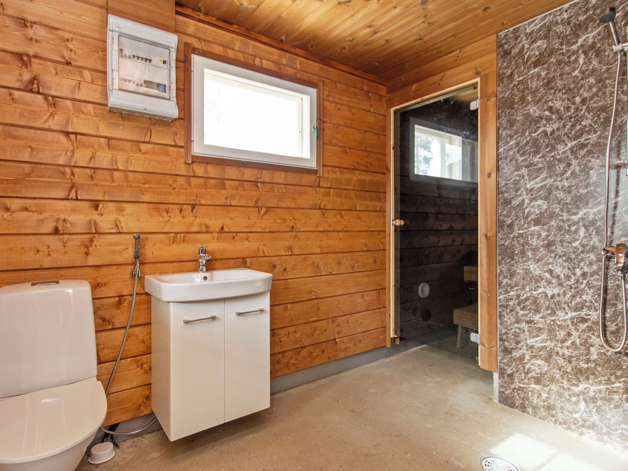 Baño de cabaña de madera con inodoro, lavamanos y ducha.
