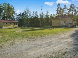 A rural property with a gravel driveway, a yellow house, and a wooden structure.