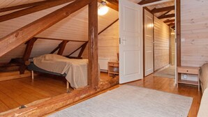 Een gezellig slaapkamer op zolder met een houten plafond, een bed, een nachtkastje en een deur naar een andere kamer.