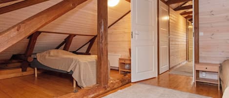 A loft bedroom with a sloped ceiling, wooden beams, a bed, a nightstand, and a door leading to another room.