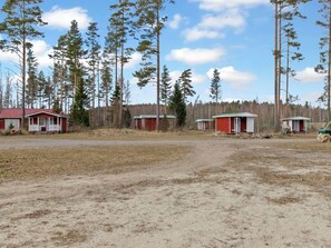 A row of cabins with a dirt ground and a forest in the background.