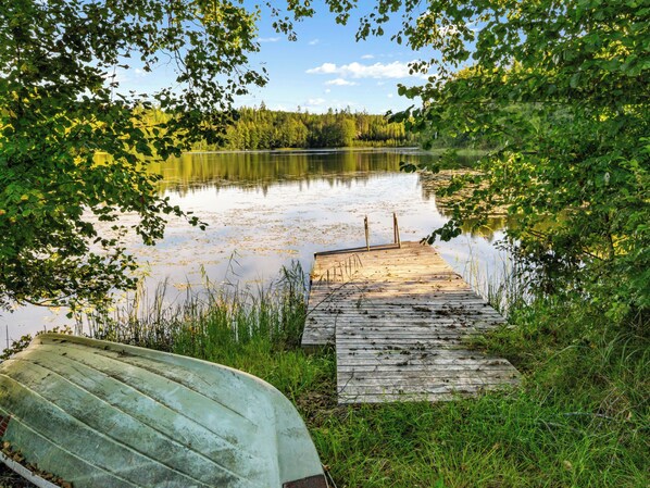 A wooden dock leading to a calm lake, surrounded by lush greenery and trees.