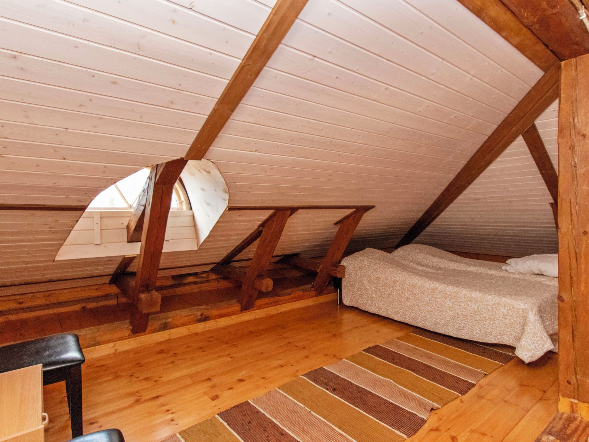 Ein kleines Schlafzimmer im Dachgeschoss mit schrägen Wänden, Holzbalken, einem Einzelbett und einem Schreibtisch.