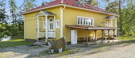 A yellow house with a red roof, a porch, and a stone in front.