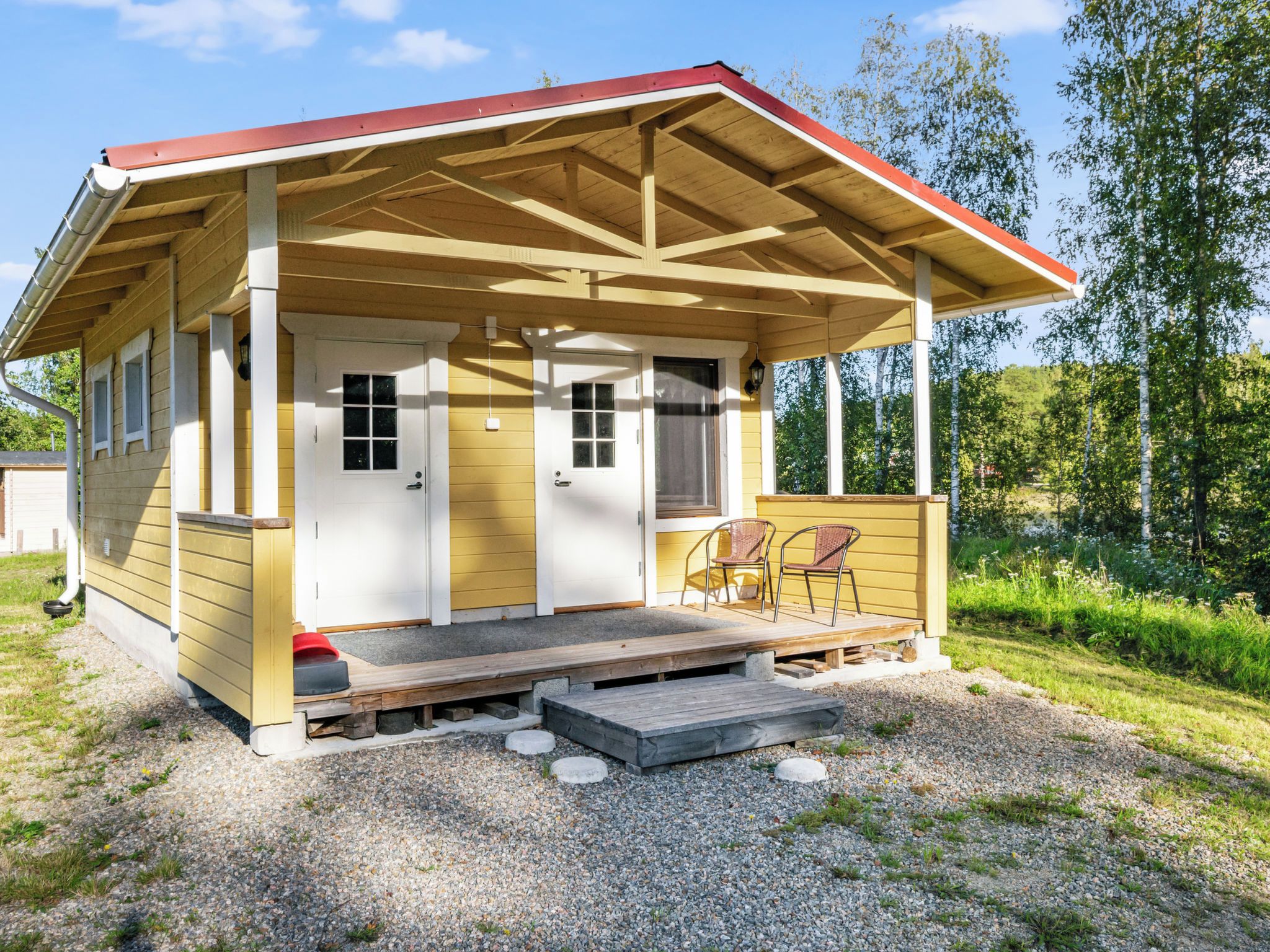 A small wooden cabin with a porch, two doors, and a seating area with two chairs.