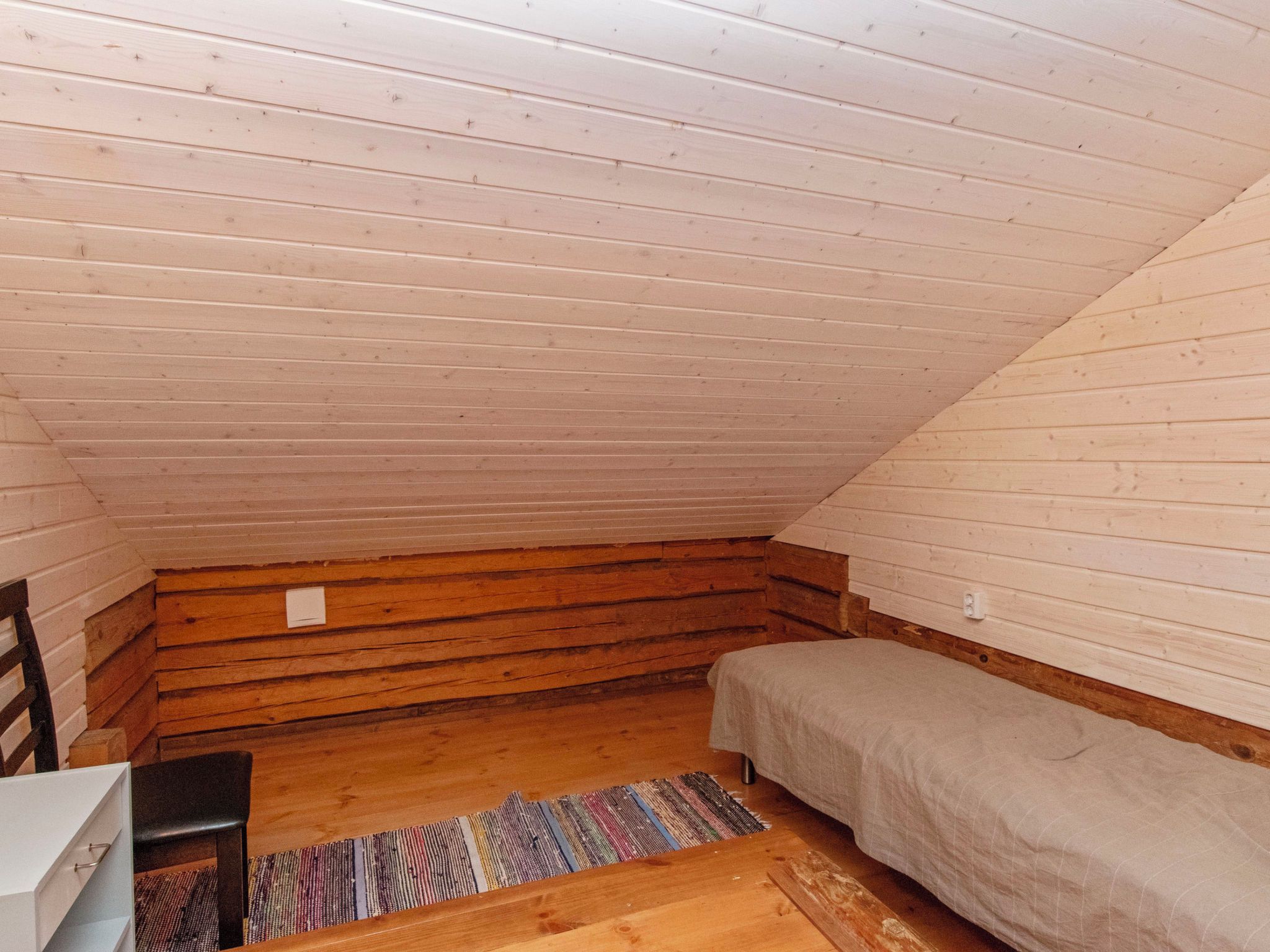 A small, single-room attic space with a sloped ceiling, a bed, a chair, and a desk.