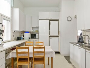 A compact kitchen with white cabinets, a dining table with chairs, a microwave, a refrigerator, and a sink.