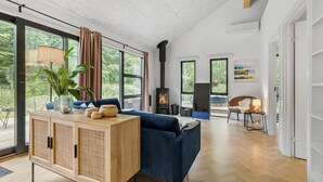 Un soggiorno moderno con una grande finestra, un divano blu, un armadietto in legno e un camino.