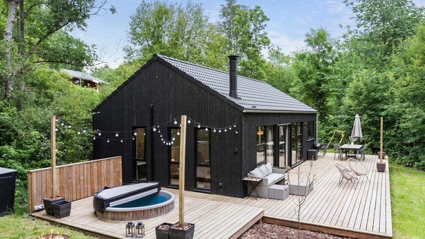 Una moderna casa nera con una terrazza, una vasca idromassaggio e posti a sedere all'aperto.
