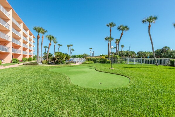 A golf course with a well-maintained green, palm trees, and a building with balconies.